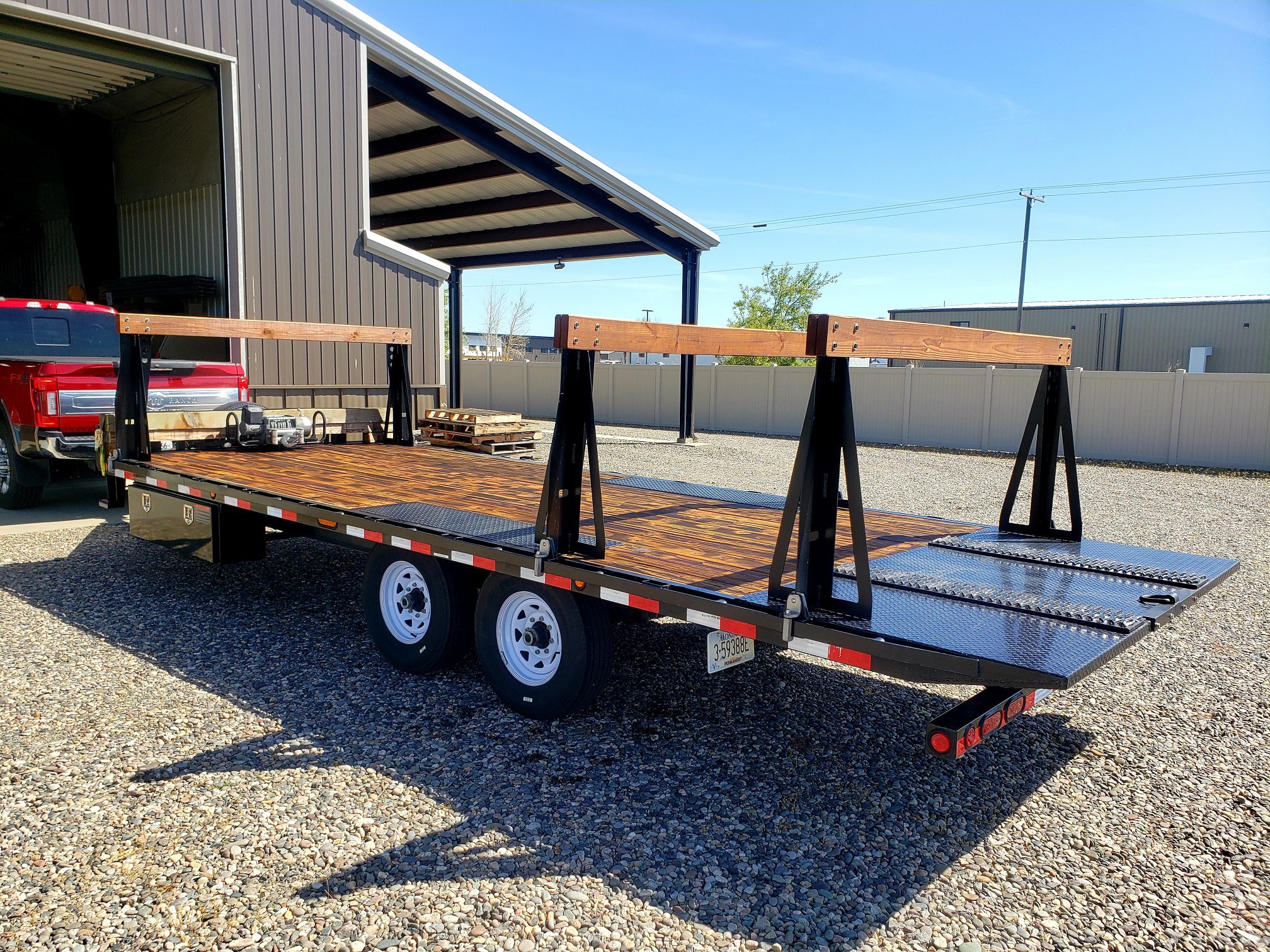 A flatbed trailer with ramps parked on gravel under a clear sky.