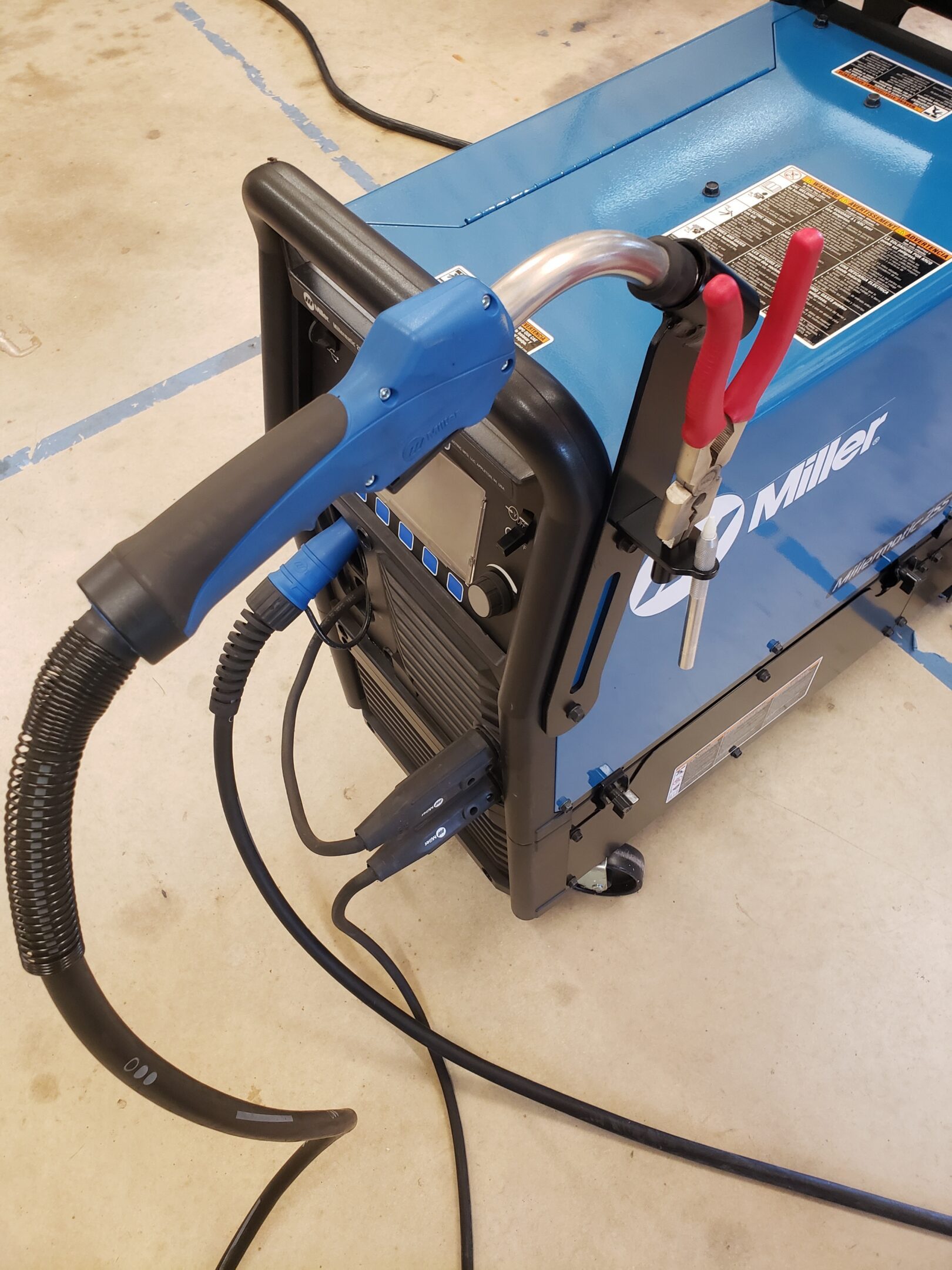 A blue welding machine with attached cables and clamps.