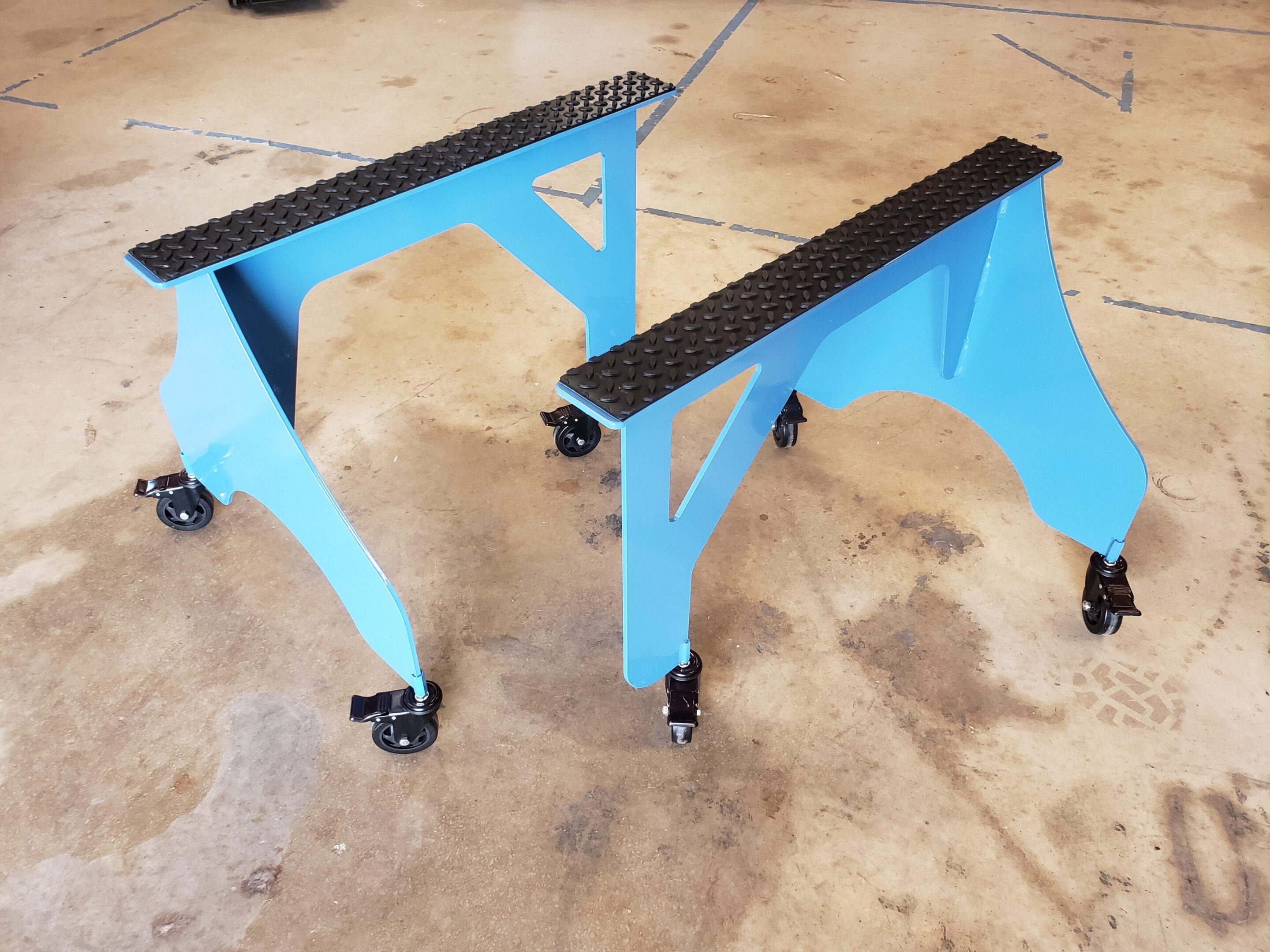 Two blue metal sawhorses with black tops on a concrete floor.