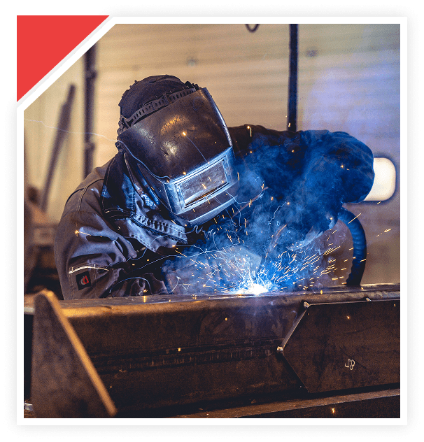 A welder in protective gear welding metal with bright sparks.