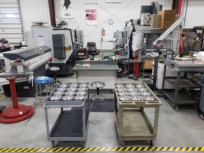 A manufacturing workspace with machines and trays of metal parts.