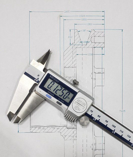 Digital caliper measuring a metal part on a technical drawing.